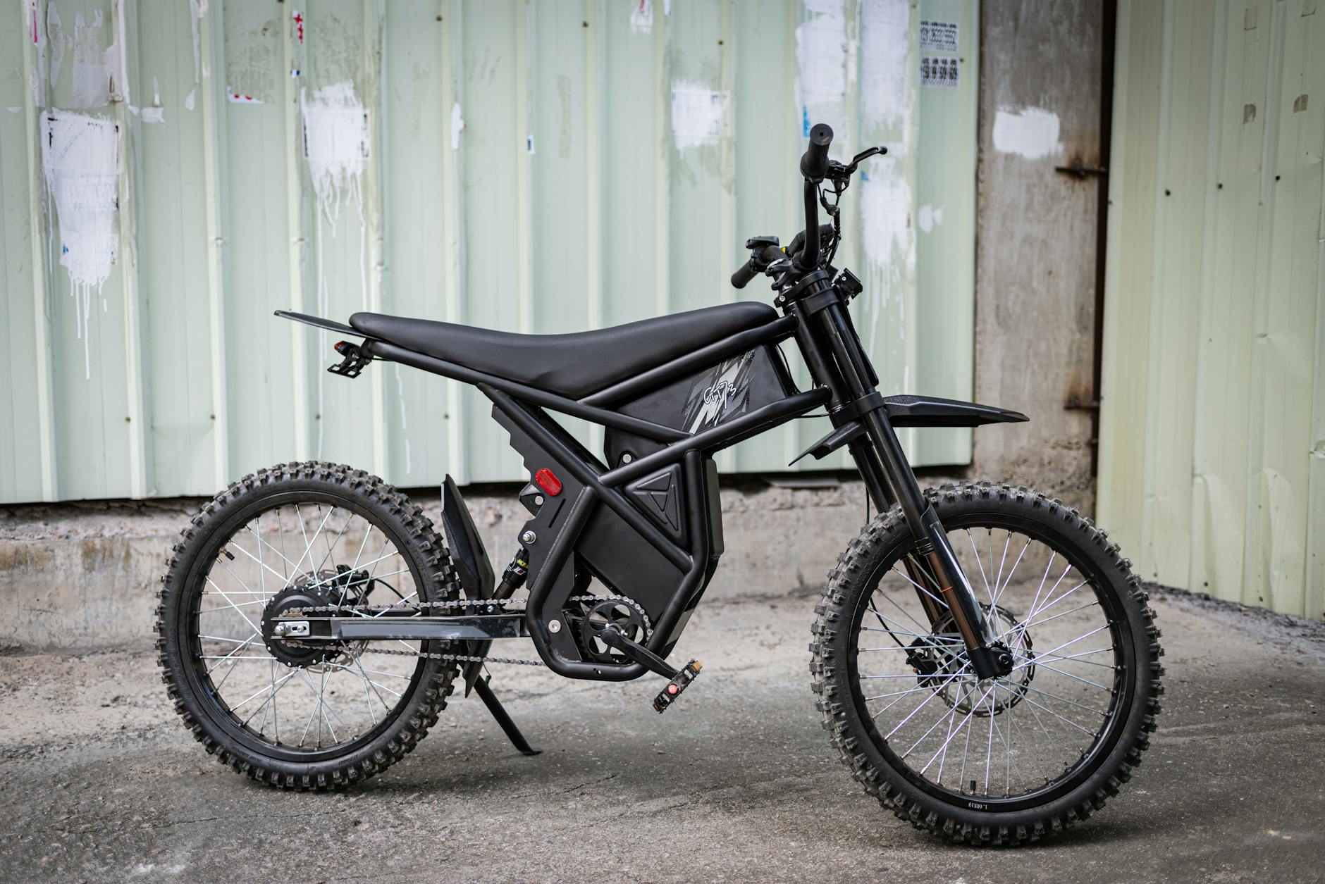 A modern black electric bike with rugged tires is parked in front of a corrugated metal wall.